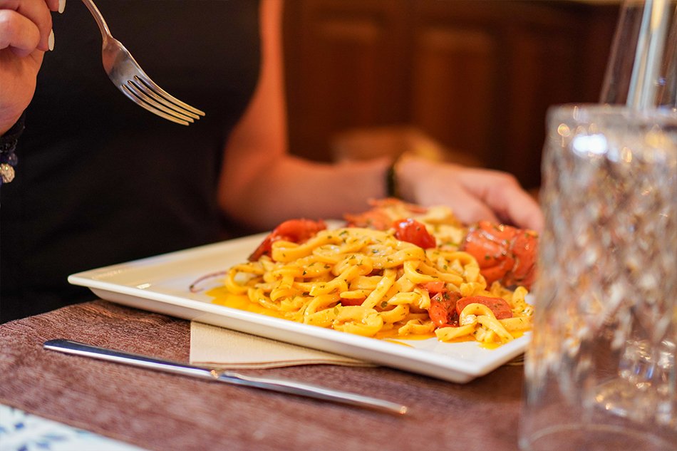 Un piatto di pasta fresca con gamberi e pomodorini appena servito in tavola, con la forchetta già in mano