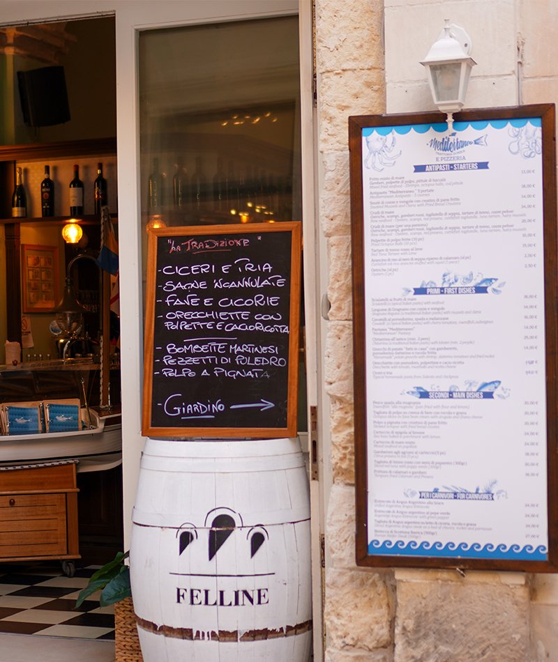 L’ingresso del ristorante in pietra leccese: la lavagna «La tradizione» scritta a gesso appoggiata su una botte bianca, e il menù esposto in italiano e inglese