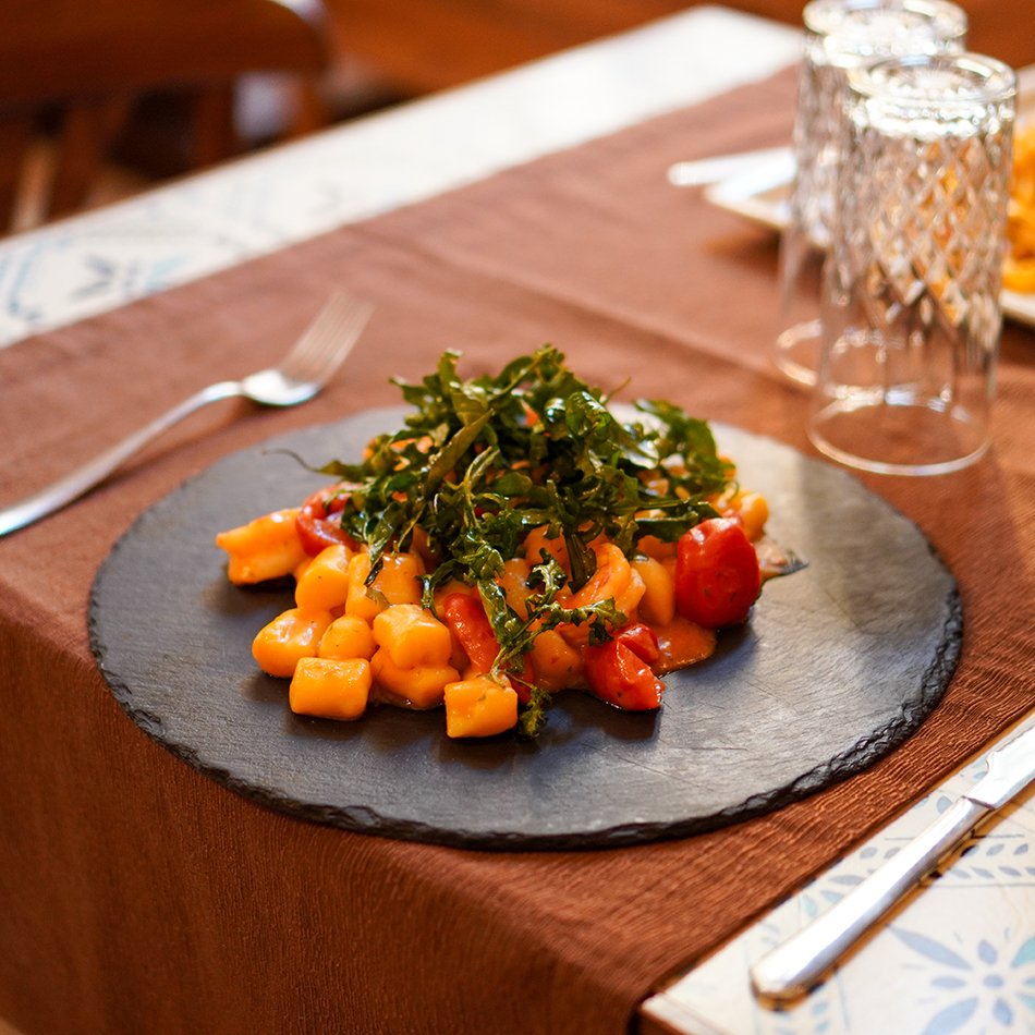 Gnocchi di patate fatti in casa con pomodorino datterino e rucola fritta, serviti su un piatto tondo di ardesia
