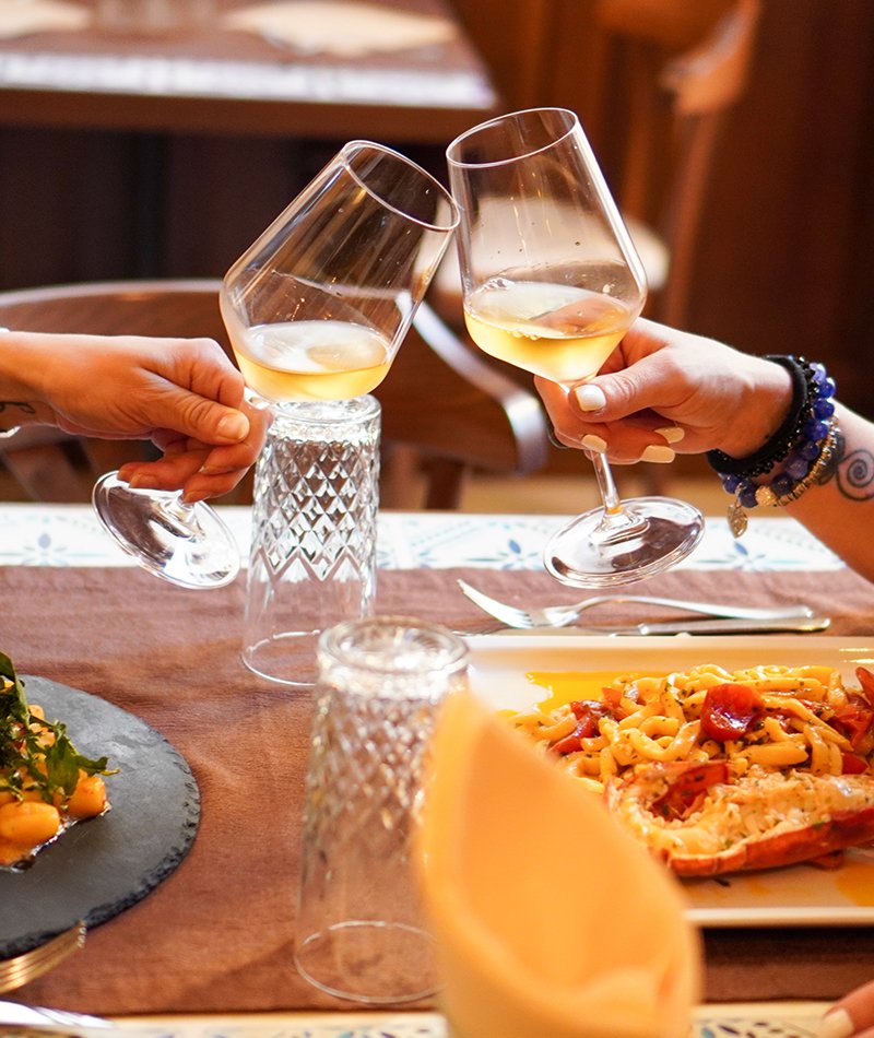 Due bicchieri di vino bianco che si toccano sopra il tavolo apparecchiato, con il runner a stampa di cementina blu e i tovaglioli gialli piegati